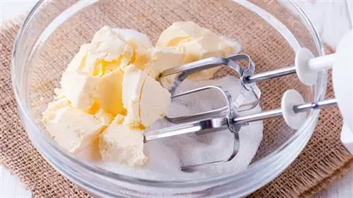 Масло и сахар в стеклянной миске с ручным миксером