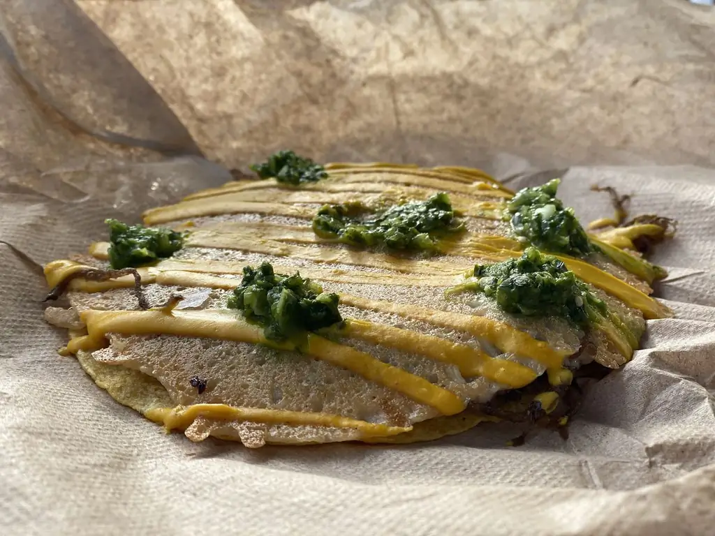 Хрустящий сыр с зелеными кружочками сальсы cruda на фиолетовом картофельном тако