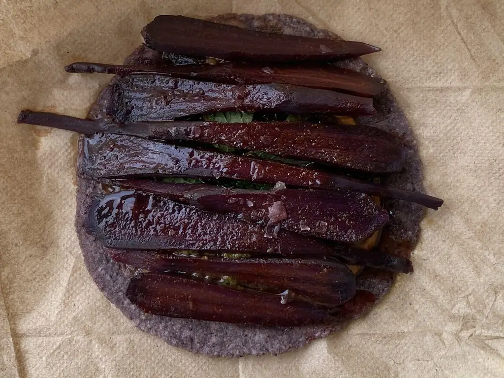 Фиолетовая морковь, посыпанная солью, сидит над тостадой из синей кукурузы