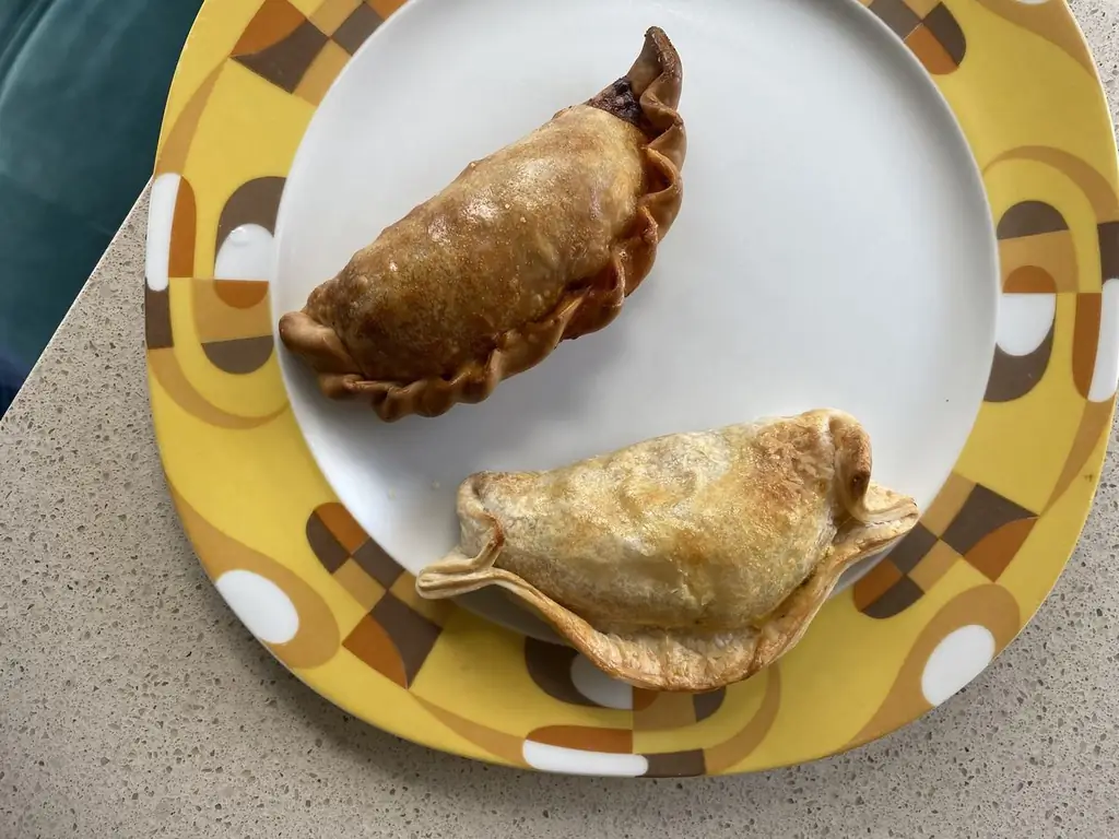 На бело-желтой декоративной тарелке лежат эмпанада из говядины цвета красного дерева и капрезе посветлее