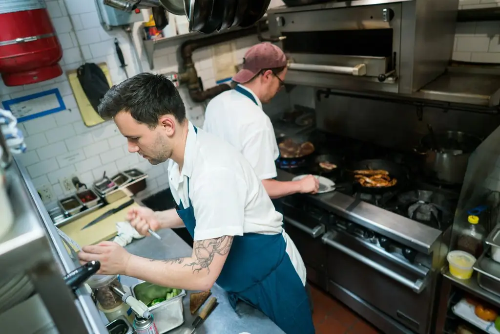Один повар готовит у плиты, а другой на переднем плане