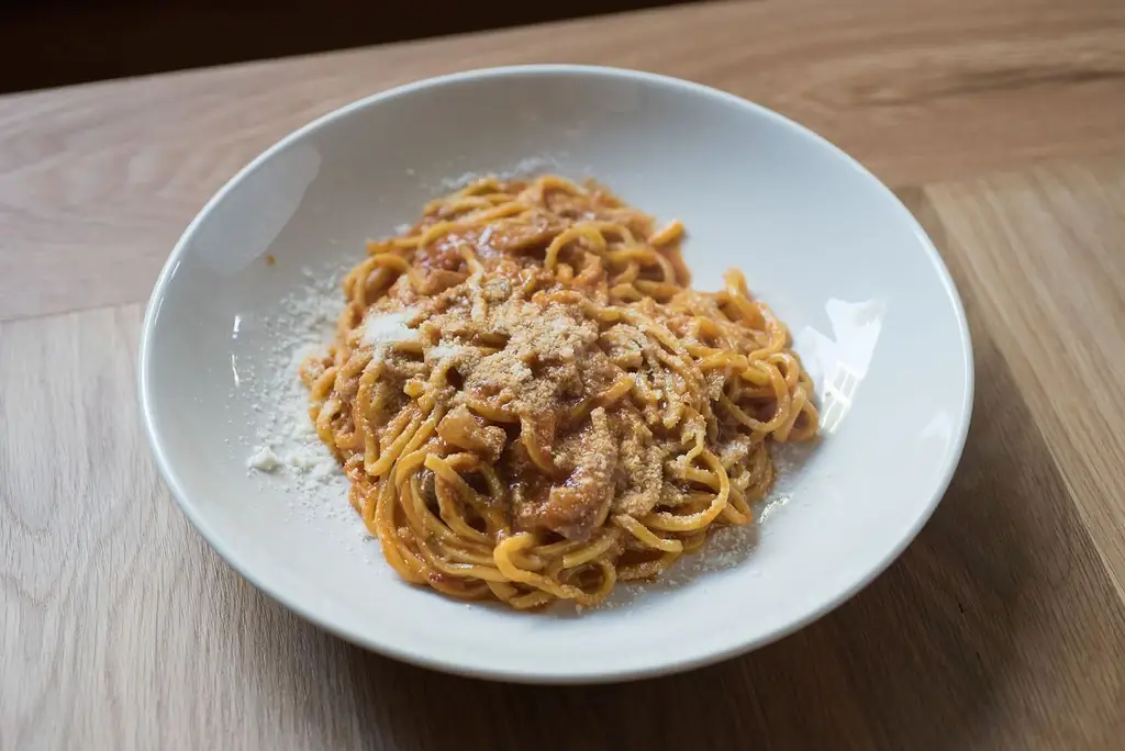 Тарелка пасты с красным соусом на белой тарелке в Уово. Tonnarelli amatriciana в Уово