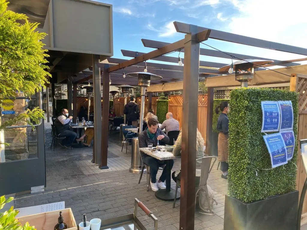 Сиденья на открытом воздухе в Нари, где посетители едят на расстоянии друг от друга, а официанты в масках. Тепловые лампы и зелень усеивают пространство