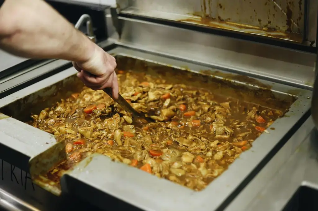 Рука, держащая большую ложку, перемешивает кастрюлю промышленного размера