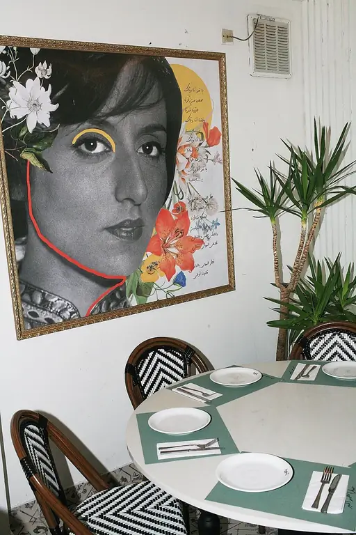 Столовая в Бейт-эль-Зайтун, с зеленой сервировкой и большой фотографией женщины на стене, в оттенках серого, но с добавлением цвета от цветов