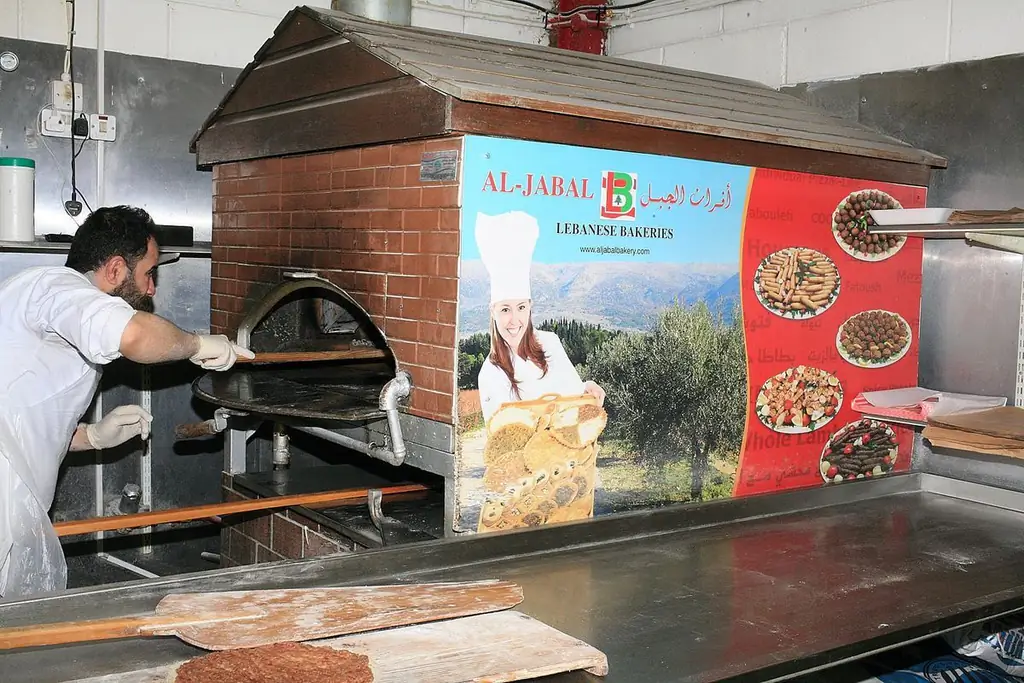 Внутри Al Jabal, с плоским man’oushe на металлической стойке и плакатом, изображающим шеф-повара с хлебом на фоне залитого солнцем дерева